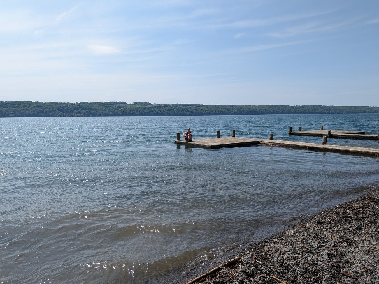 Lake shoreline with a wooden dock extending into the water under a clear blue sky.