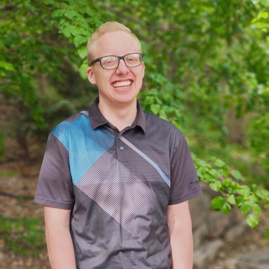 Smiling man wearing glasses and a patterned polo shirt outdoors
