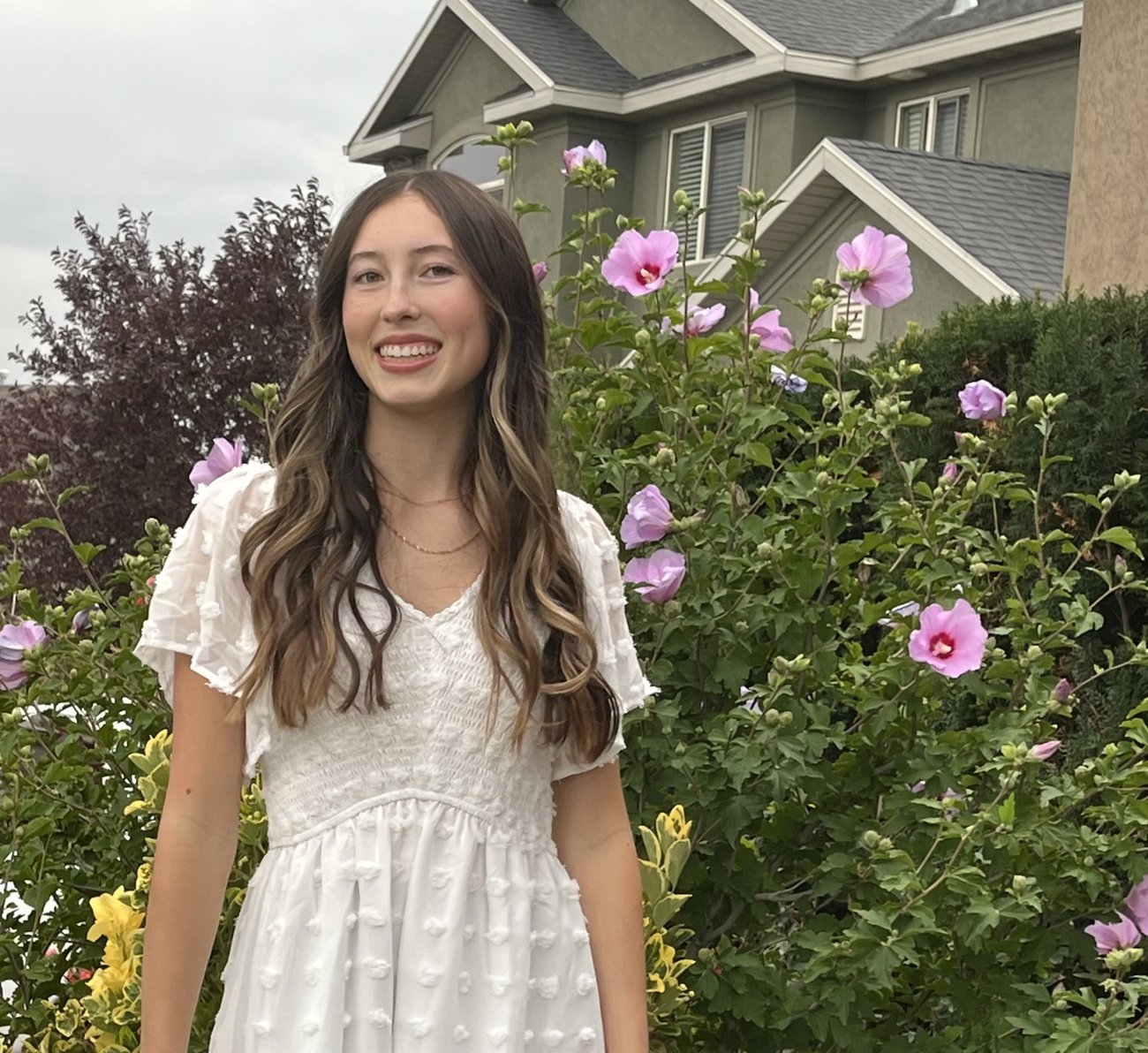 Smiling woman in a white dress standing among pink flowers