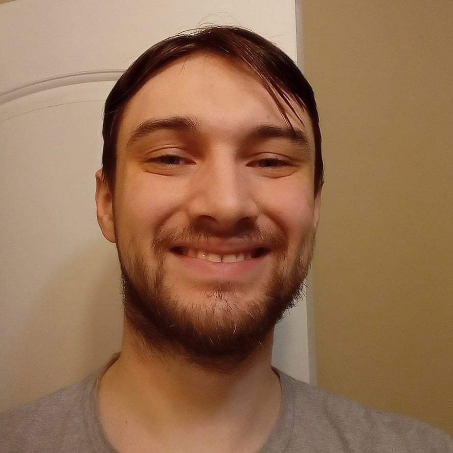 A smiling bearded man with brown hair wearing a gray shirt