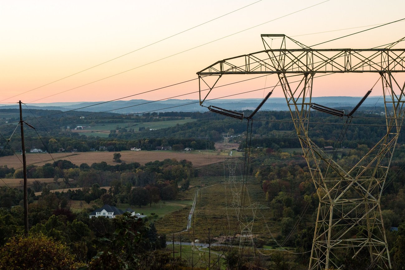 A view of the sky, mountains, trees, and power lines taken from high ground.