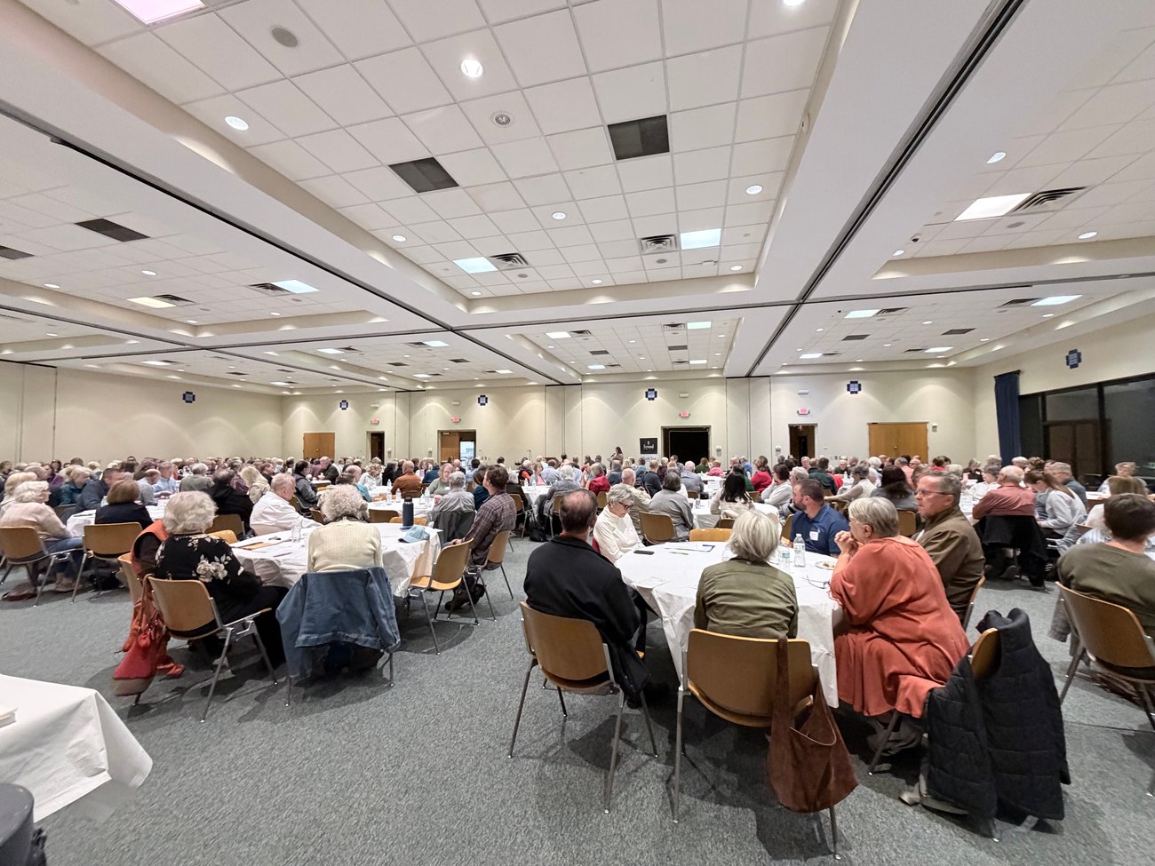 A large group of people seated at tables in a bright mirrored dining room
