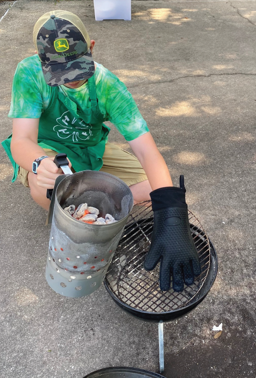 4-H youth holding bucket of food next to grilll