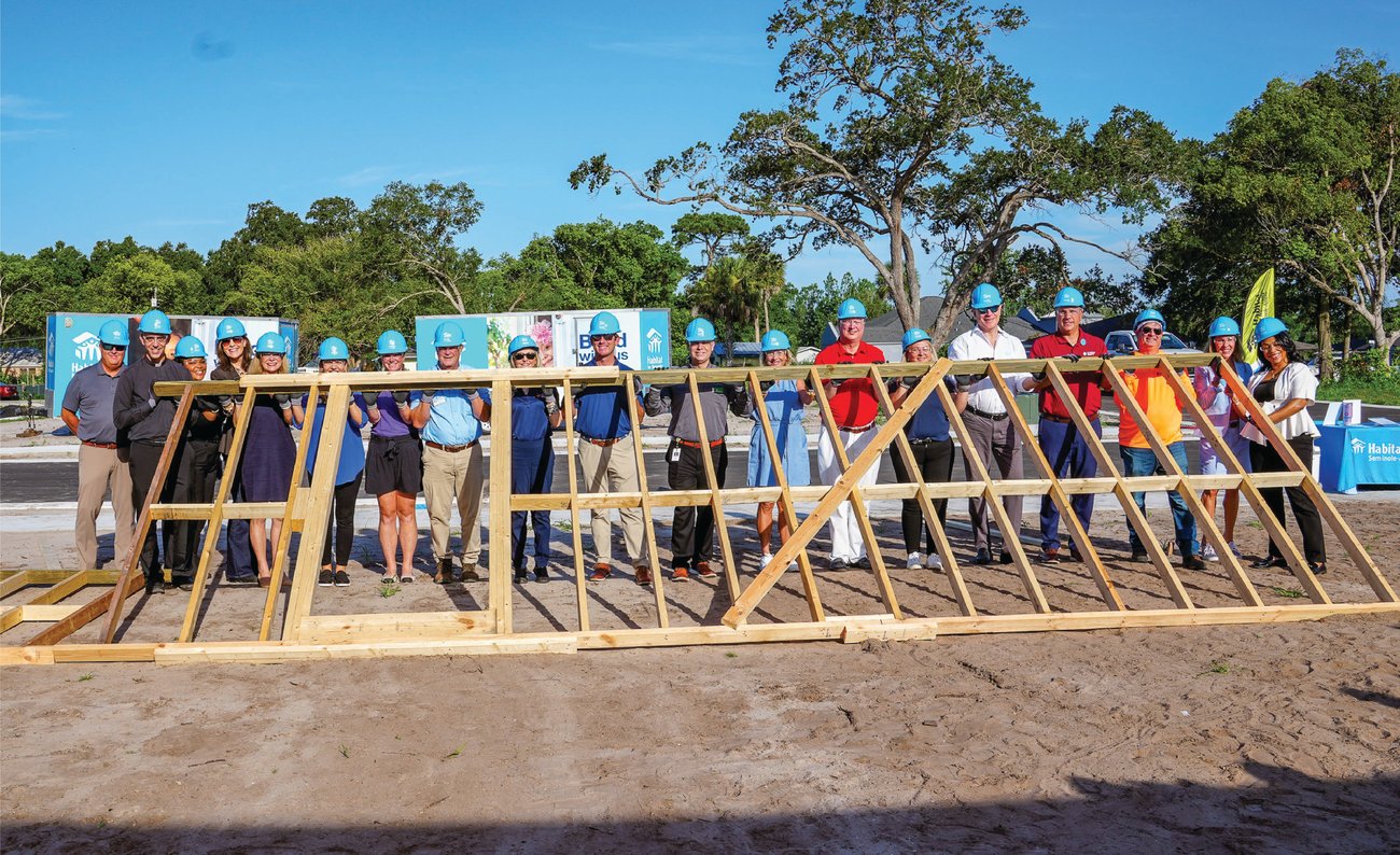 large group of people wearing construction helmets posing on dirt lot with wood house frame large group of people wearing construction helmets posing on dirt lot with wood house frame