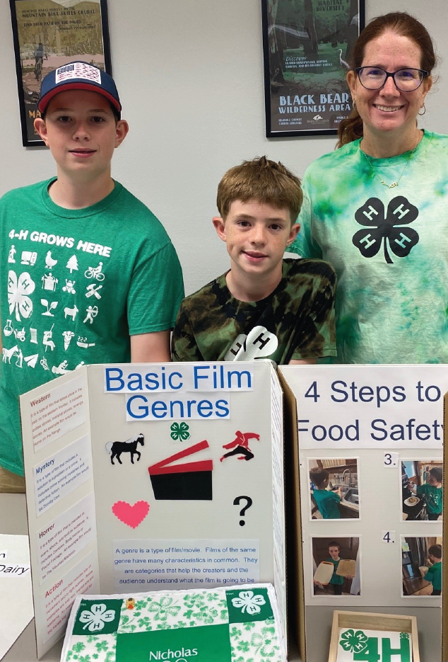 2 boys standing next to woman at information booth with poster props in front on table