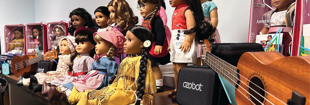 group of dolls sitting and standing on a table, with ozobot toy and ukuleles next to them group of dolls sitting and standing on a table, with ozobot toy and ukuleles next to them