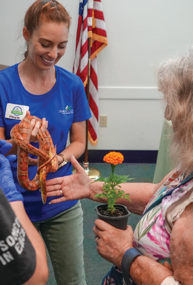 2 women holding an orange snake and flower