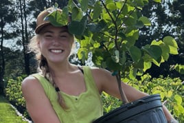 Smiling woman holds a leafy plant outdoors in bright sunlight