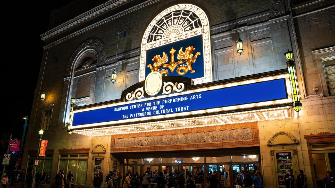 A brightly lit theater marquee at night reads, Benedum Center for the Performing Arts, A Venue of the Pittsburgh Cultural Trust. People are gathered near the entrance under the lights. A brightly lit theater marquee at night reads, Benedum Center for the Performing Arts, A Venue of the Pittsburgh Cultural Trust. People are gathered near the entrance under the lights.