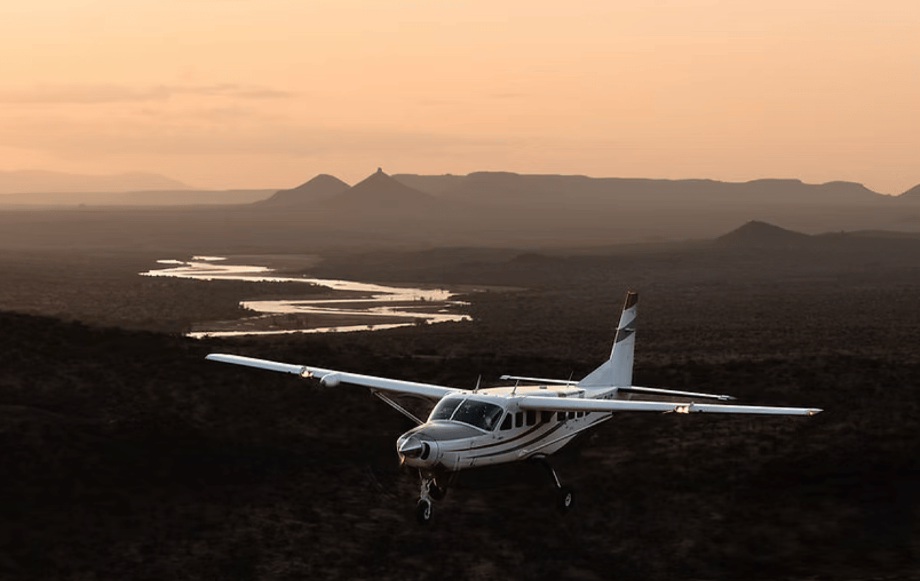 Small airplane flying over dark terrain with mountains and a sunset sky Small airplane flying over dark terrain with mountains and a sunset sky