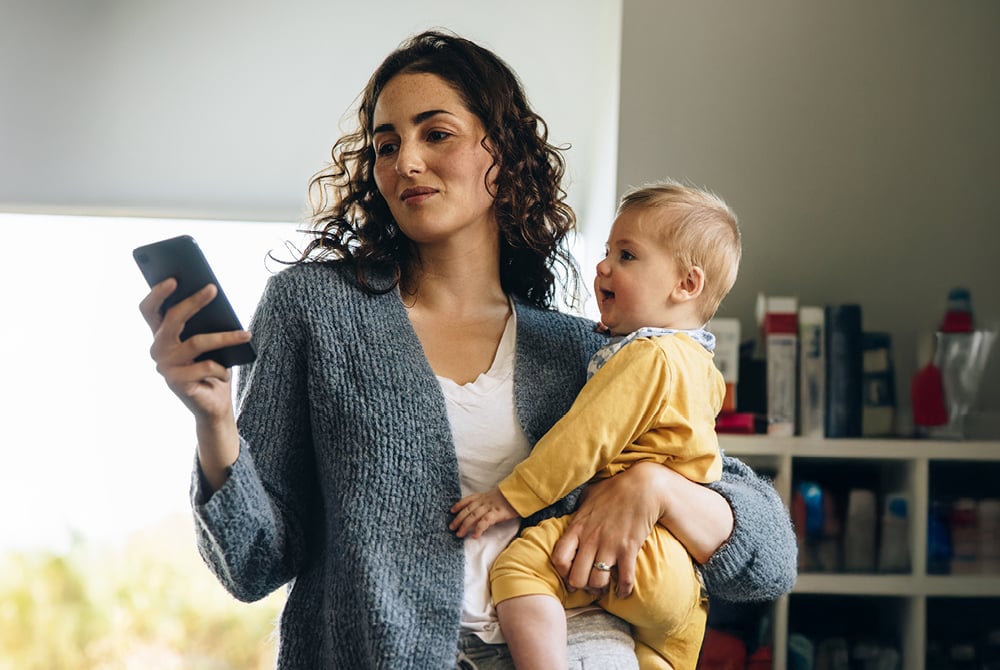 Woman texting on her phone while holding a baby