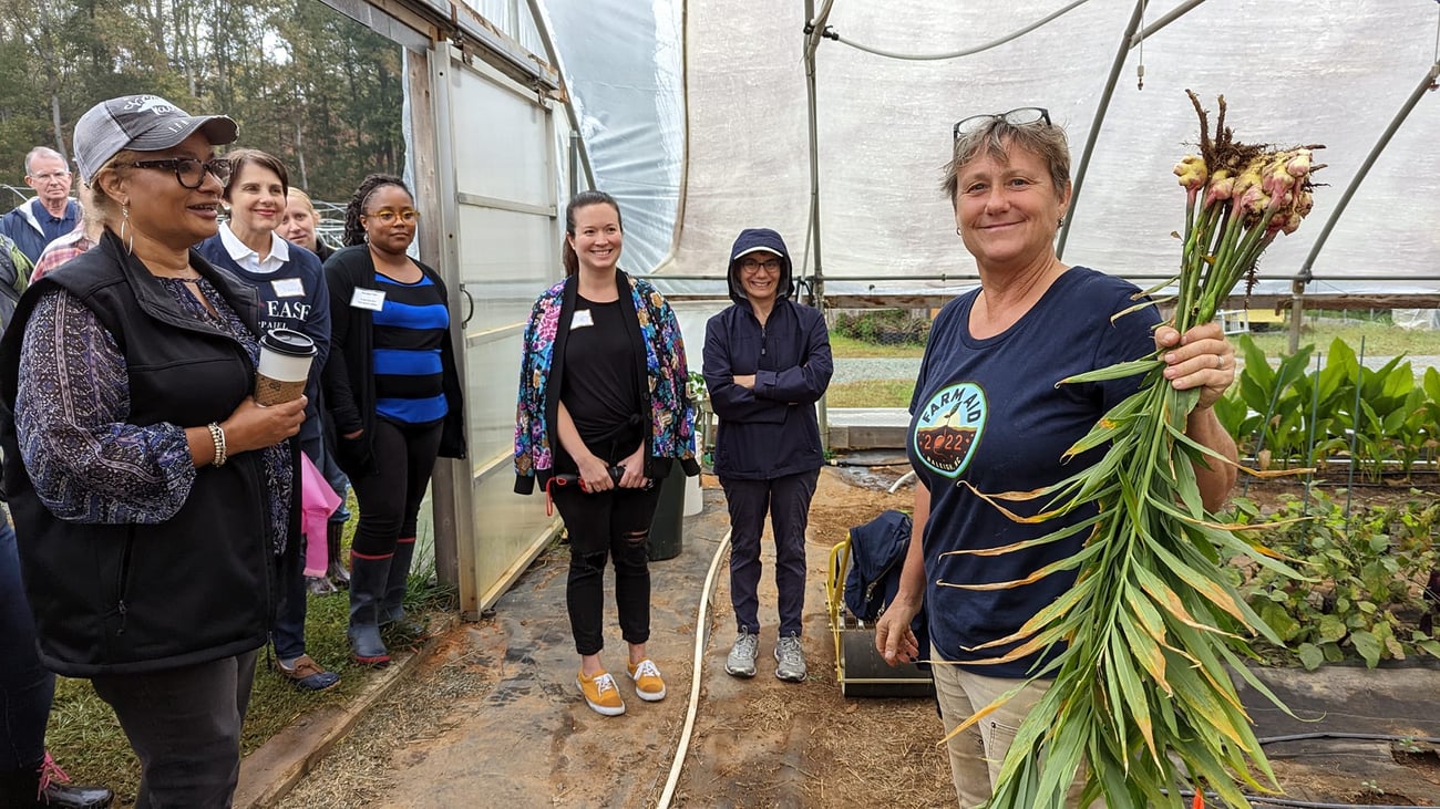 Several folks gathered around a farmer in a greenhouse ,showing a root of a plant. Several folks gathered around a farmer in a greenhouse ,showing a root of a plant.