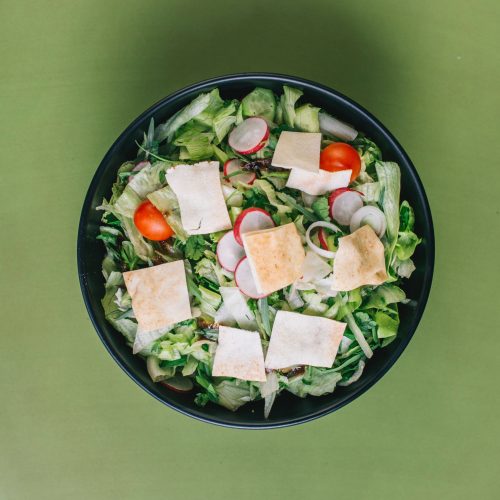 A salad with a mix of vegetables in a black bowl.