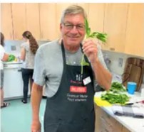 An older man with glasses holding a green plant in his left hand.