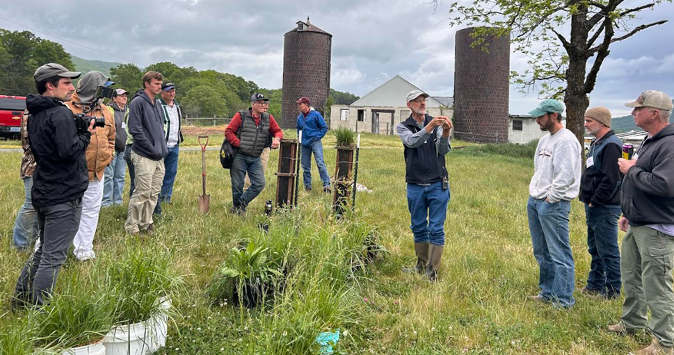 NC State Extension ruminant specialist Matt Poore stands in a farm field with silos in the background, speaking to a crowd of farmers during an Extension field day.