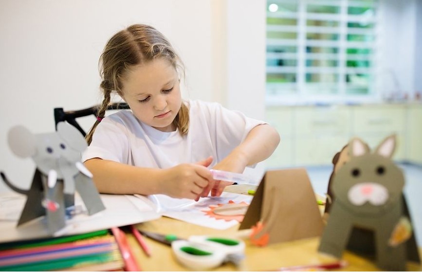 Young girl sitting at a table doing crafts with paper and scissors Young girl sitting at a table doing crafts with paper and scissors