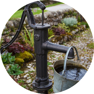 A manual well pump with a bucket of water hanging from it.