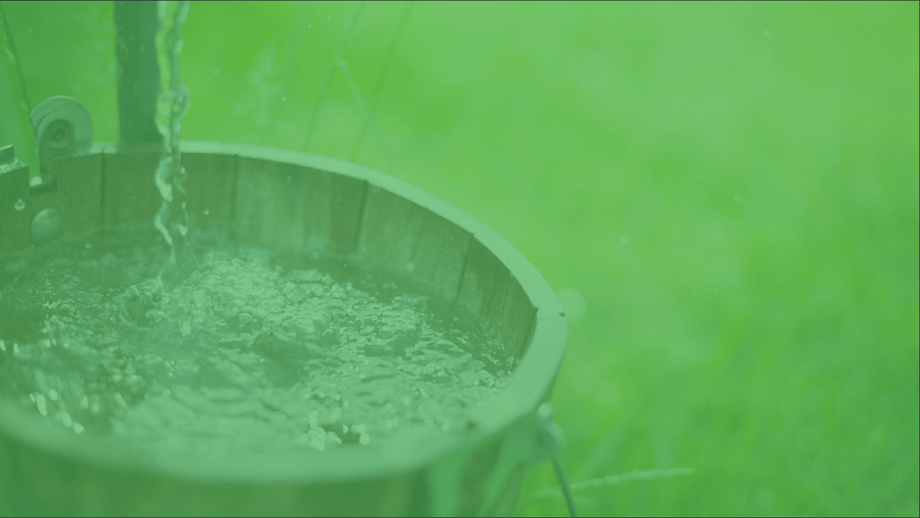 A water bucket being filled with water from a manual well pump.
