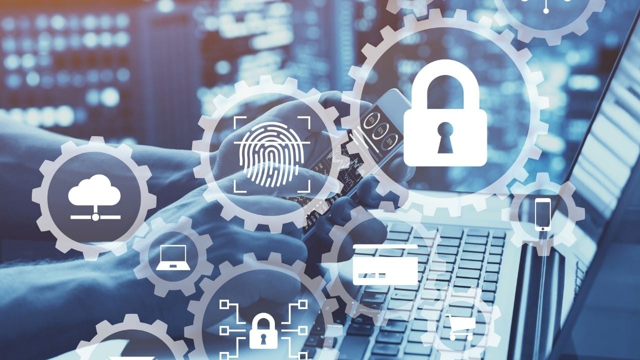 Header image of gears with cybersecurity related icons overlayed on a photo of a person holding a phone in front of an open laptop screen