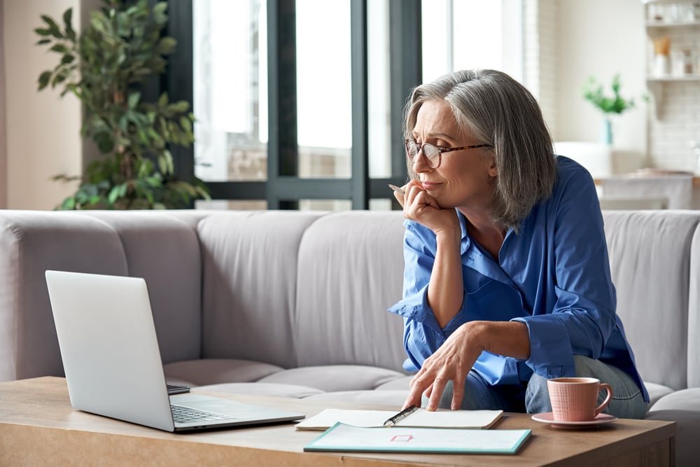 A woman sitting on a sofa looking at the laptop screen in front of her