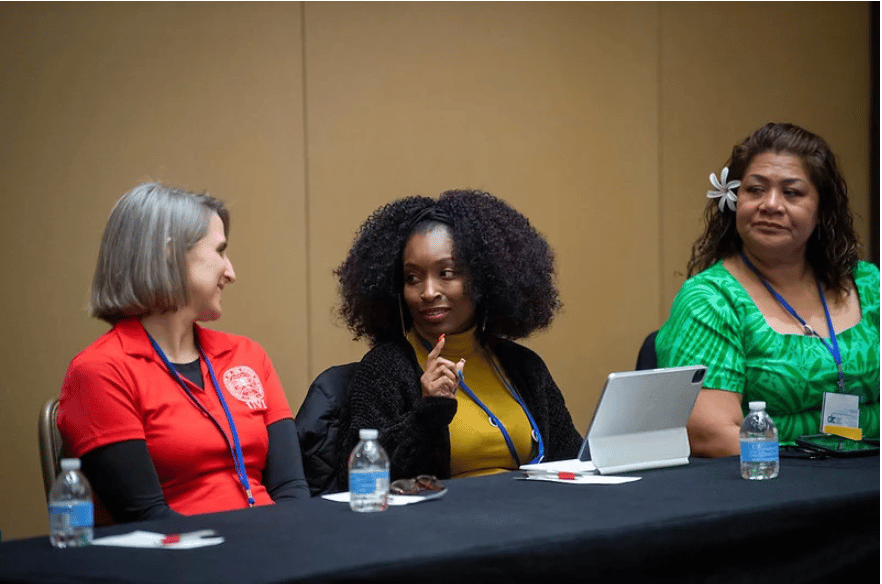 Three women behind a table conversing.