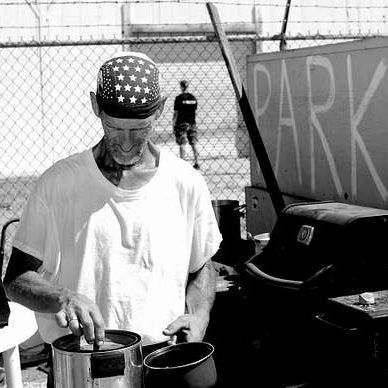 Homeless man stirring something in a pot.