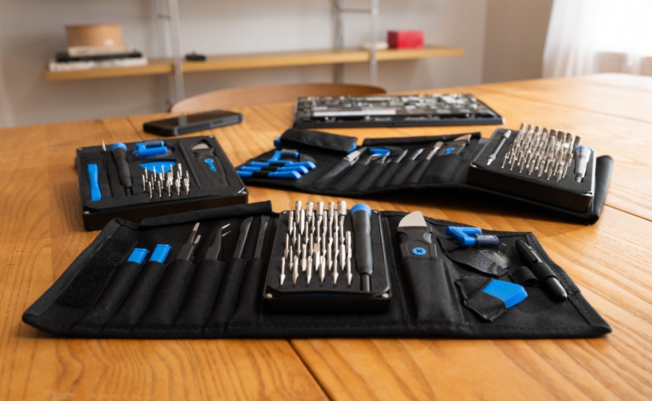 Several open iFixit toolkits are displayed across a wooden table, showing organized bits, drivers, and repair tools in a bright indoor workspace.