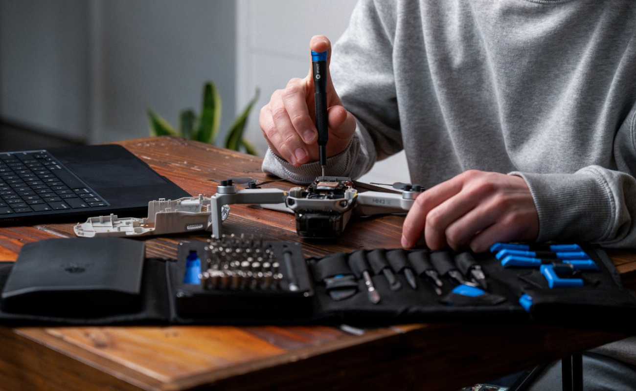Hands repairing a drone with the Pro Tech® Toolkit open beside it, with a laptop in the background.