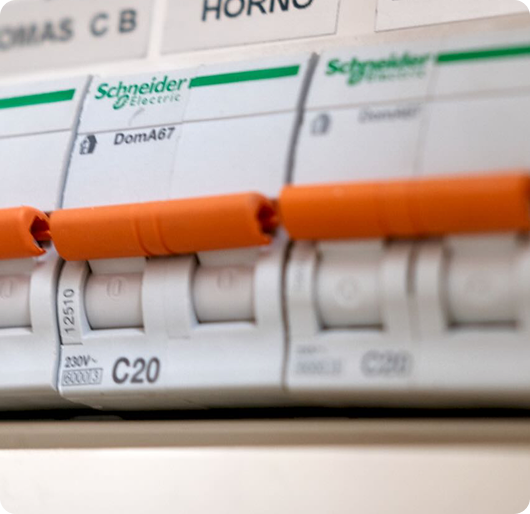 Close-up of a circuit breaker panel with white switches and an orange safety rail running horizontally across the foreground. The shallow-focus composition emphasizes one labeled breaker while the surrounding labels and switches fade softly into the background.