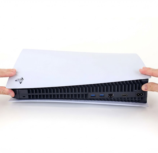 Front view of hands lifting the white outer cover from a PlayStation 5 console against a plain white background, revealing the black vented interior and rear ports