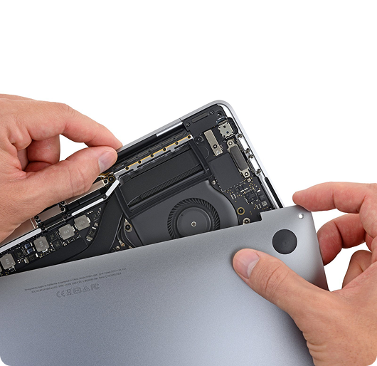 Close-up of hands removing the bottom cover from an open MacBook laptop
against a white background, revealing the internal cooling fan, battery, and circuit boards.