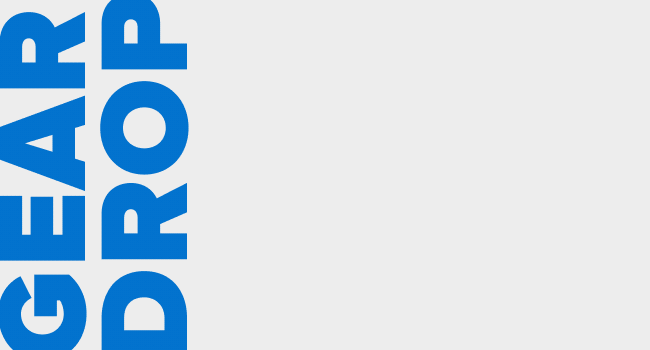 Animated graphic with large blue “GEAR DROP” lettering stacked vertically along the left, while a selection of iFixit T-shirts and a black cap slide into view across a light gray background