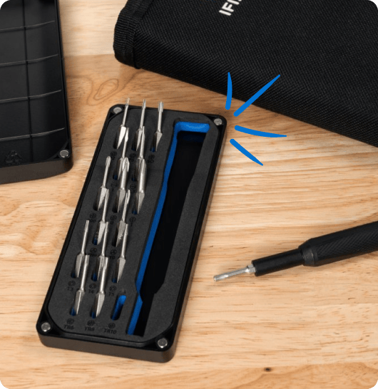 Pro Tech Essentials precision-bit case with 16 bits and an empty driver slot sits on a wooden table beside the driver handle and a black tool roll. Blue accent lines highlight the case.