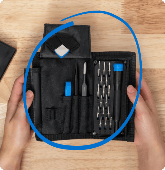 Two hands hold open a compact black tool roll containing a precision-bit set, opening tools, and small accessories on a wooden table. A thick blue circle surrounds and highlights the organized toolkit.