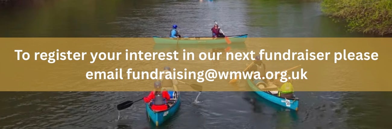 Aerial view of several people paddling canoes along a river surrounded by greenery. A gold banner across the centre of the image contains white text that reads: “To register your interest in our next fundraiser please email fundraising@wmwa.org.uk”. The image promotes participation in a future fundraising event.