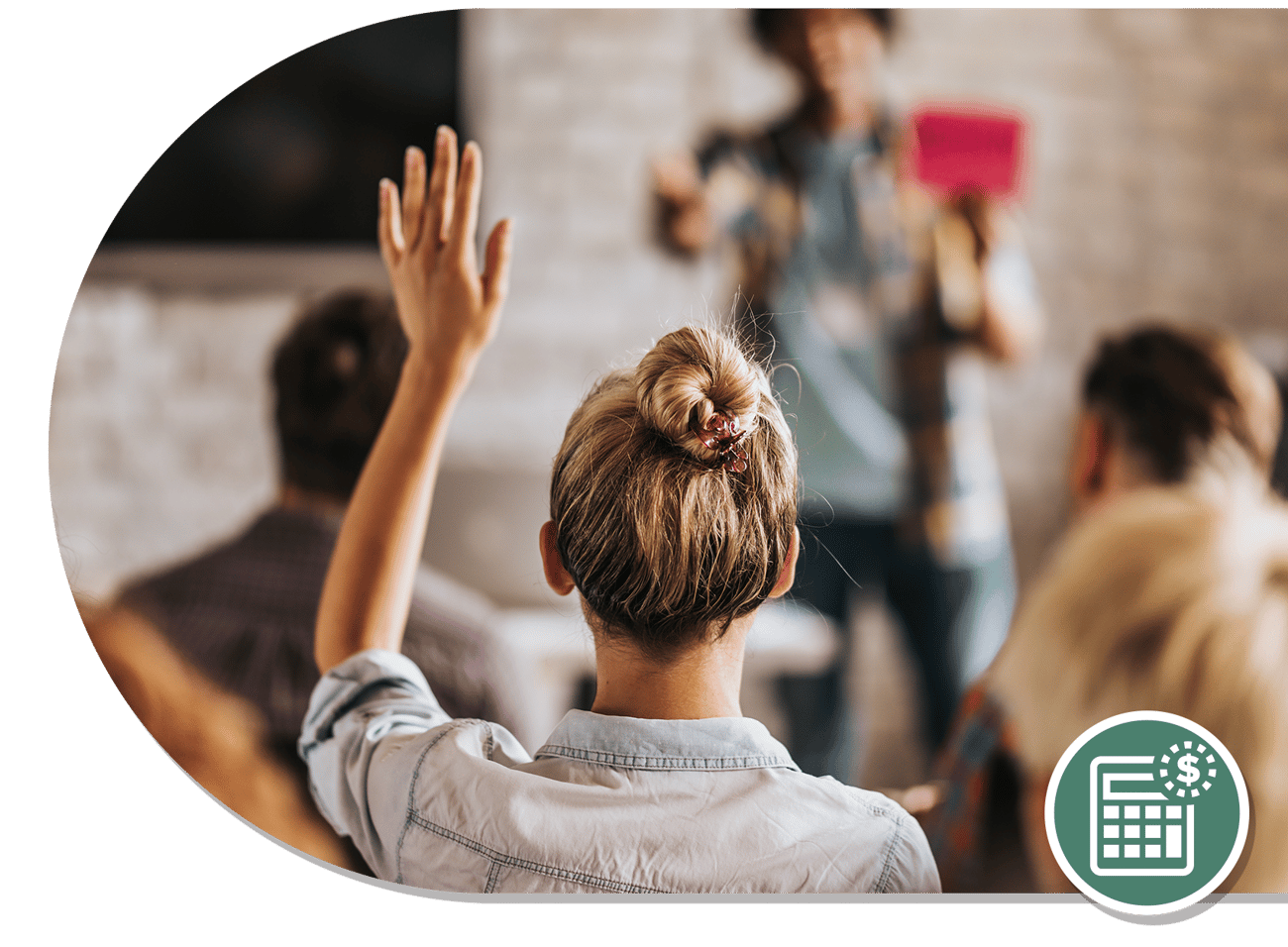 A woman with a bun raises her hand in a classroom setting while an instructor gestures at the front with a red card.