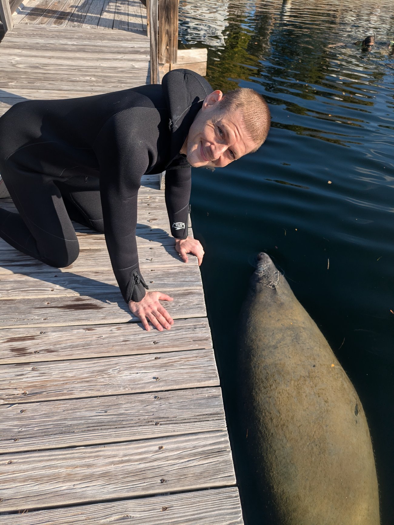 Photo of Dr. Gleb on a wooden dock with a manatee swimming by