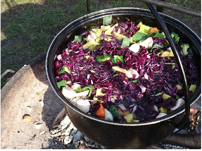 Foto einer bunten Suppe in einem Topf über einem Lagerfeuer.