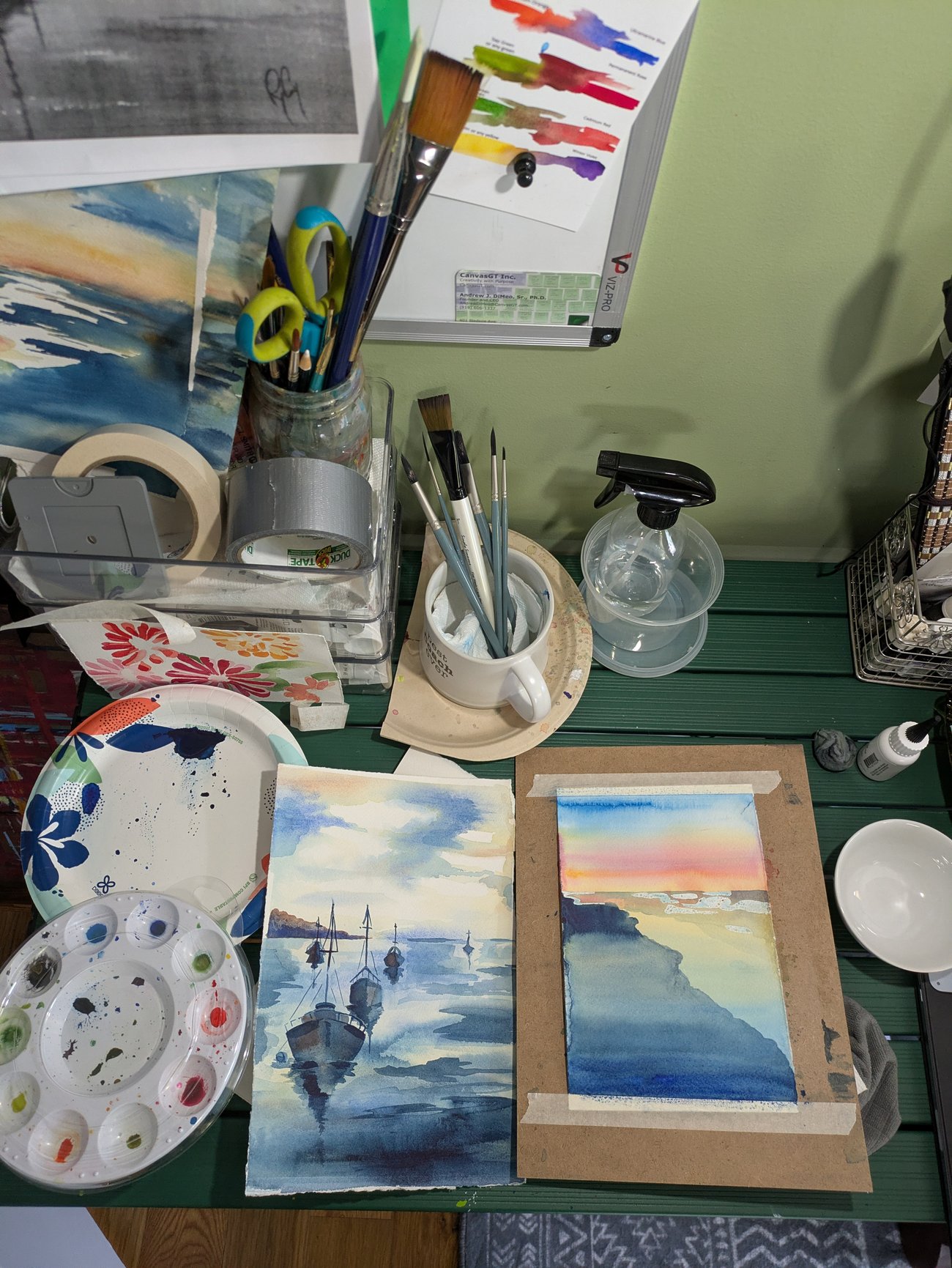 Desk with watercolor supplies and two small landscape paintings in progress.