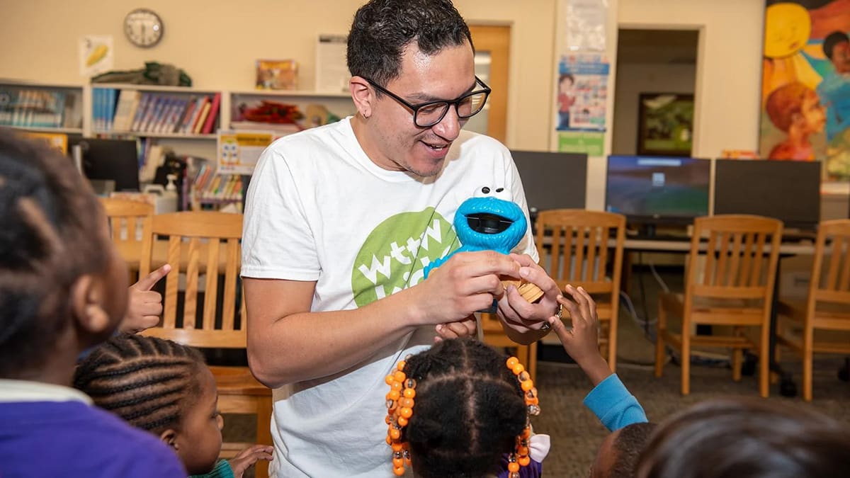 A man in a white shirt holds a toy, engaging with a group of attentive children around him. A man in a white shirt holds a toy, engaging with a group of attentive children around him.