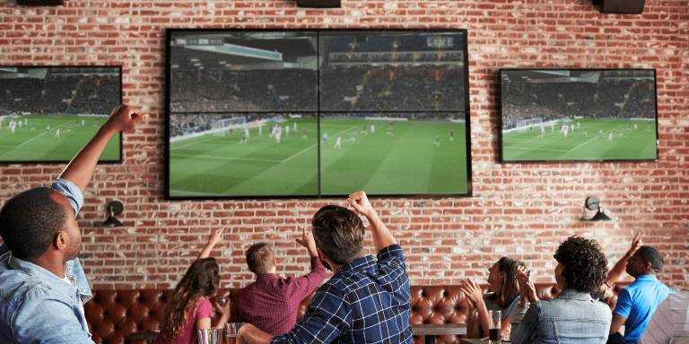 Photo of people in a restaurant watching a soccer game and cheering.