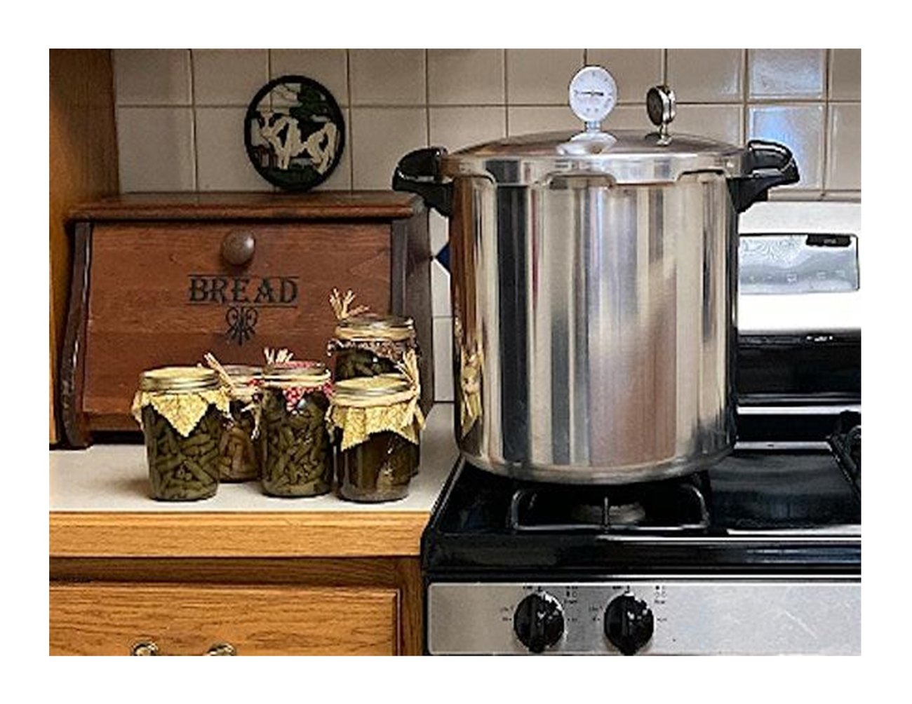 silver canner sitting on a stove with several jars of veggies sitting beside canner