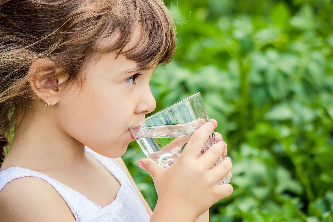 A young girl drinking a glass of water outside.