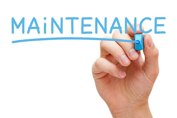 A hand holding a blue pen that has just written the underlined word "Maintenance."