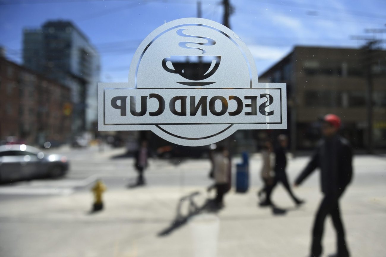 A view looking out of a window to a street where people are walking. The middle of the image has a Second Cup coffee shop logo backwards.