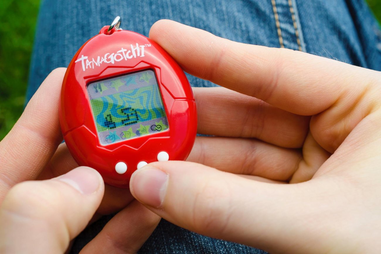 A closeup photo of hands holding a red Tamagotchi.