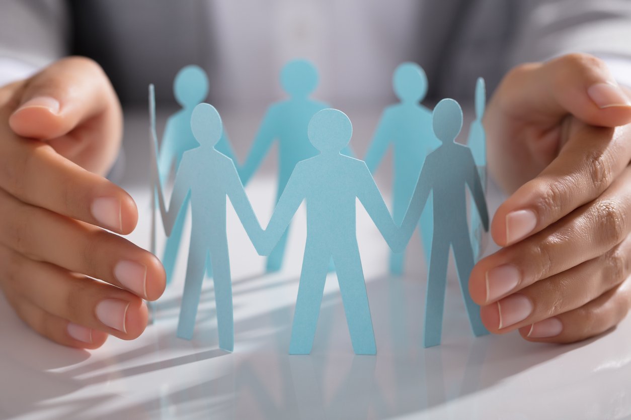 A persons hands surrounding paper cutout of people in a protective manner