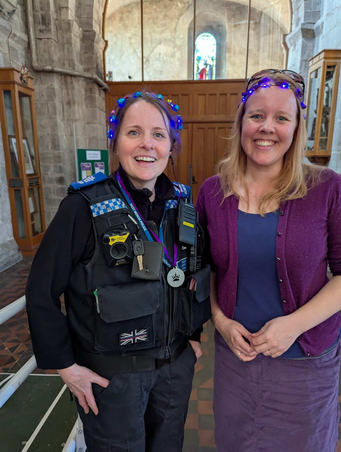 A police officer and a woman wearing purple accessories smiling together inside Leominster Priory during the Go Purple Parade community event.