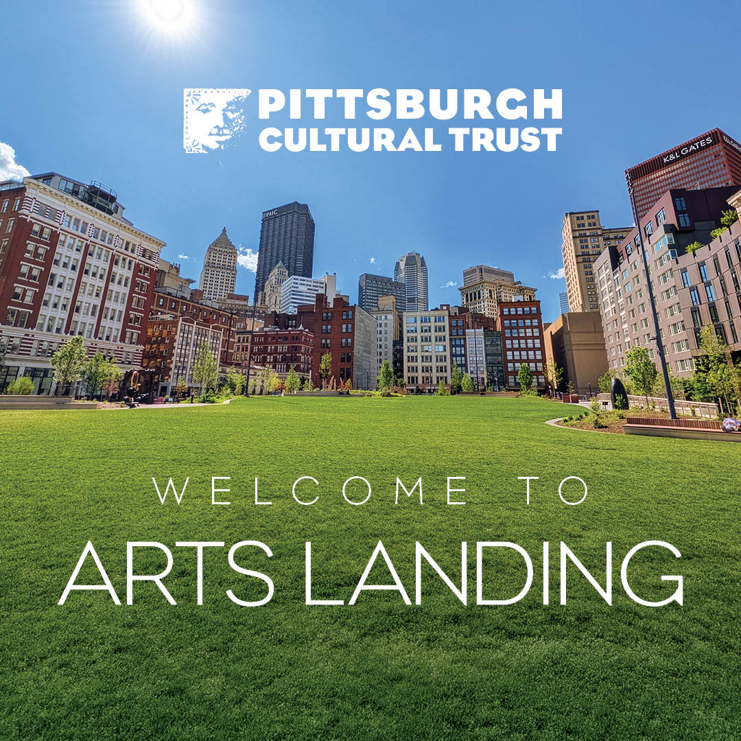 A wide green lawn with modern city buildings in the background under a clear blue sky. White text reads Welcome to Arts Landing.