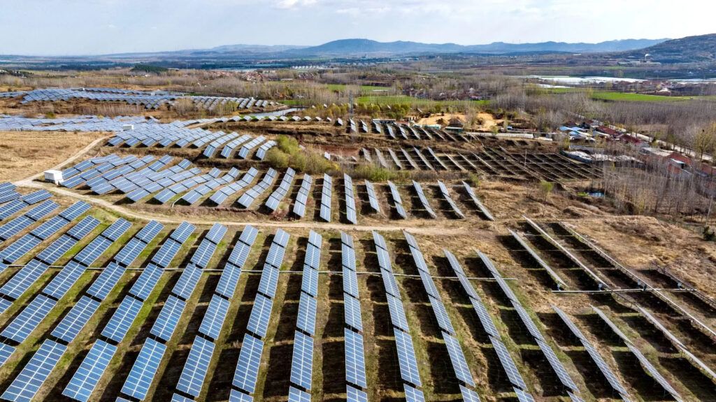 A vast field of solar panels appears in a field with mountains far off in
the distance.